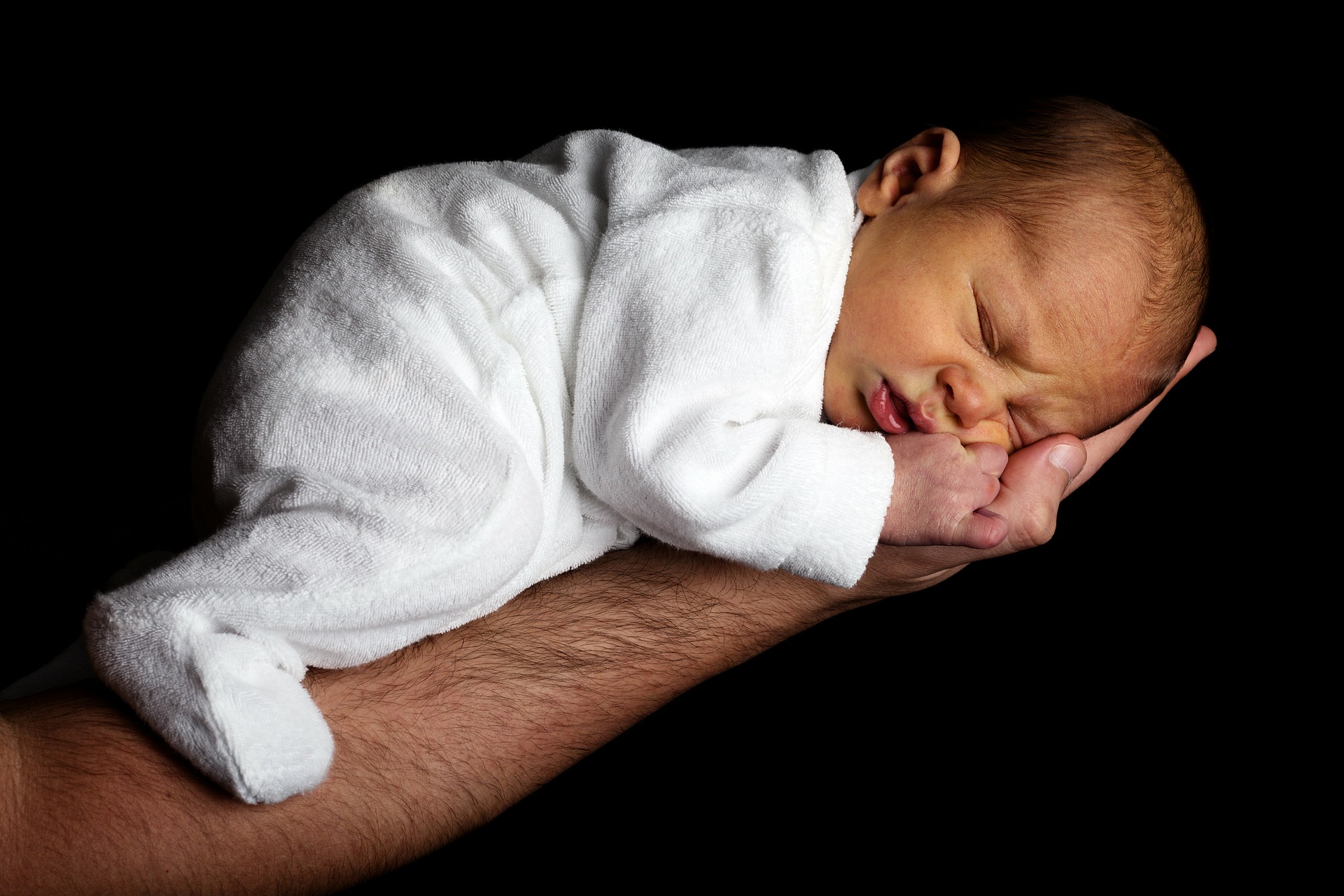baby in white dress sleeping on a man's forearm