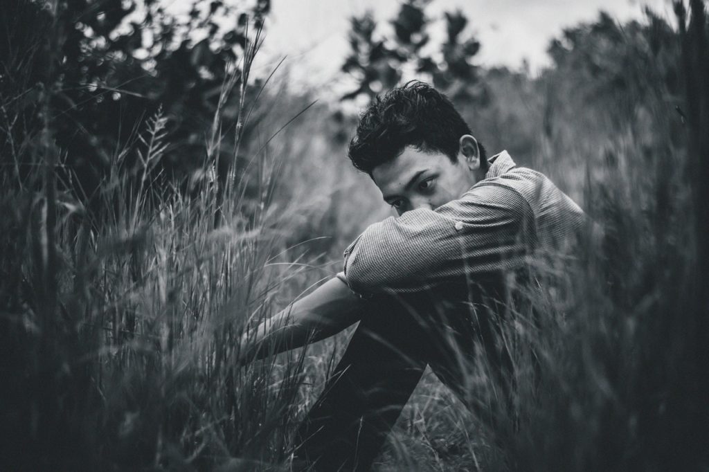 Black and white picture of depressed Teenager sitting in field